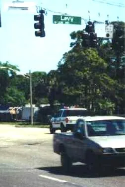 Eine Straßenkreuzung in Florida, oben in Spanndrähten hängt eine Ampel, daneben das Straßenschild, weiße Schrift auf grünem Untergrund.
