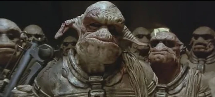 Mehrere bewaffnete Aliens mit spitzen, seitlich abstehenden Ohren, breitem Maul, wulstigen Lippen und wulstigen Augenbrauen.