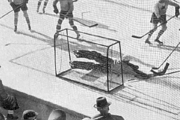 Ein Eishockeytorwart liegt vor dem Tor am Boden, rundherum angreifende Spieler.